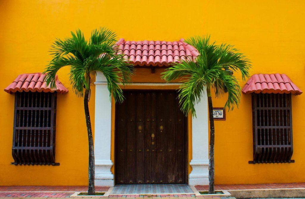 A colorful Colombian house facade with palm trees and a wooden door, tours en Colombia, destinos turísticos Colombia