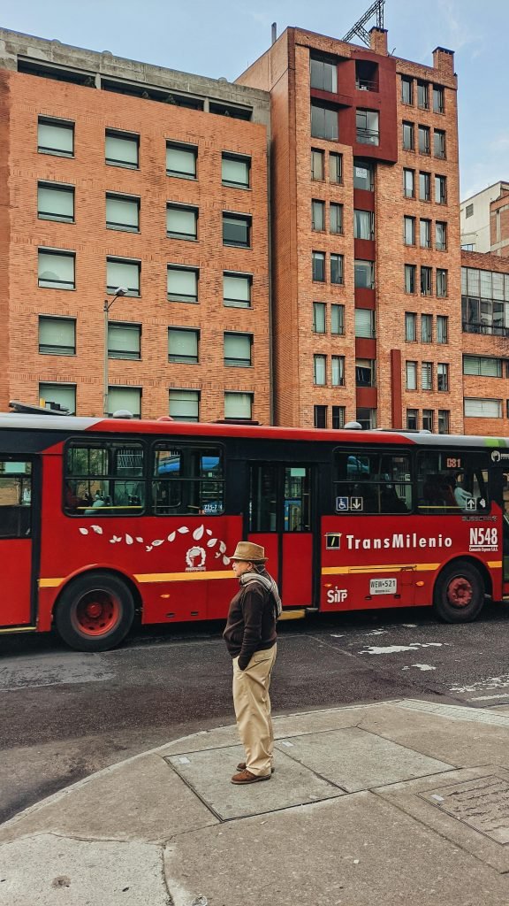 A man stands on a sidewalk next to a TransMilenio bus in Bogotá, Colombia, Planes en Bogotá