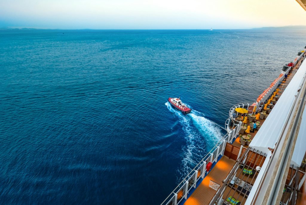 Aerial view of a luxury cruise ship with a small boat on a vast ocean at sunset, cruceros