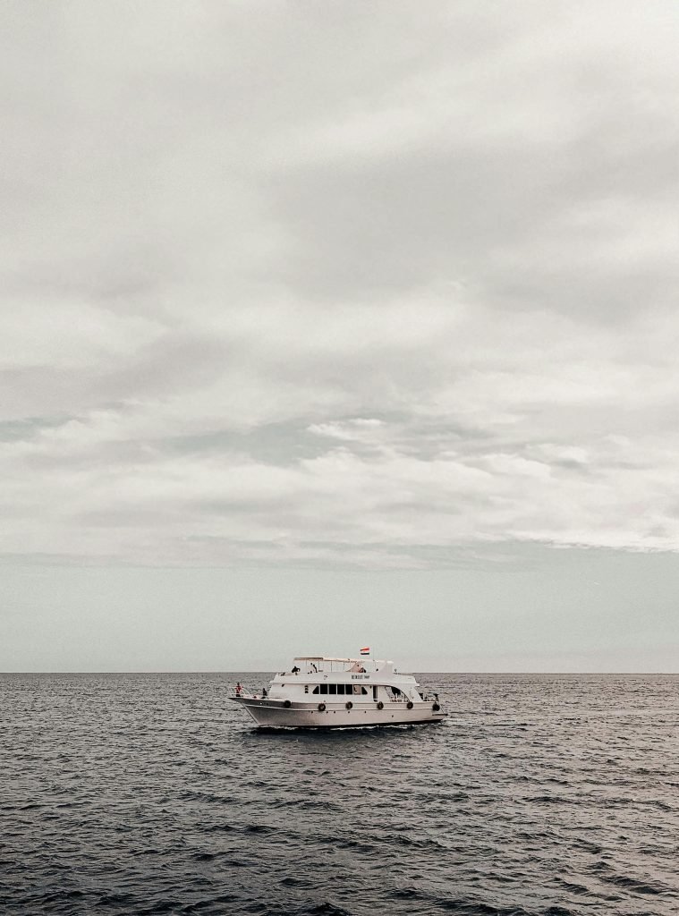 A solitary yacht floats peacefully on the ocean under a vast, cloudy sky, cruceros