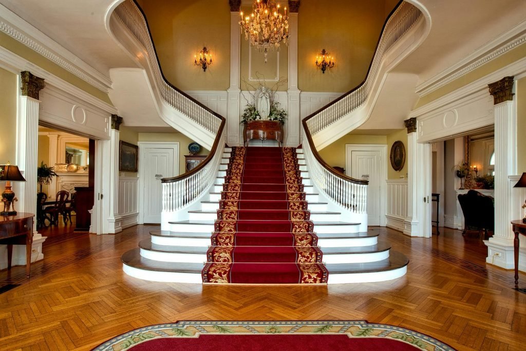 Grand staircase with red carpet in a luxurious hotel lobby, highlighted by a chandelier., hotelería