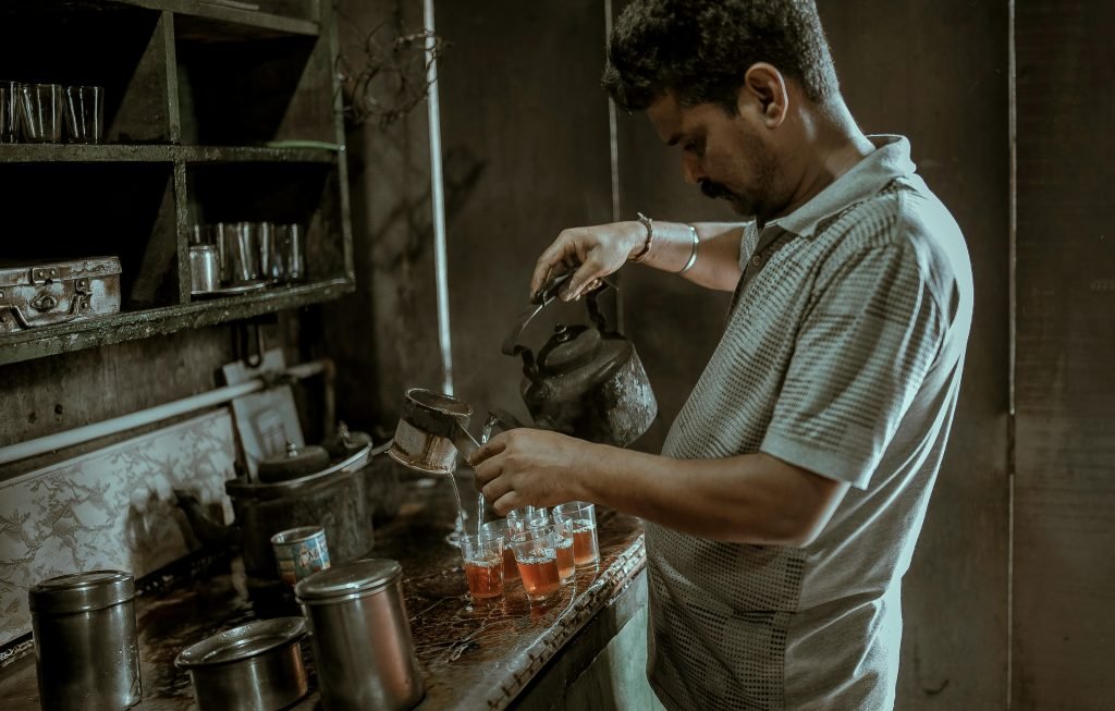 An Indian man pouring tea in a rustic kitchen setting, showcasing a cultural tea-making moment., hotelería