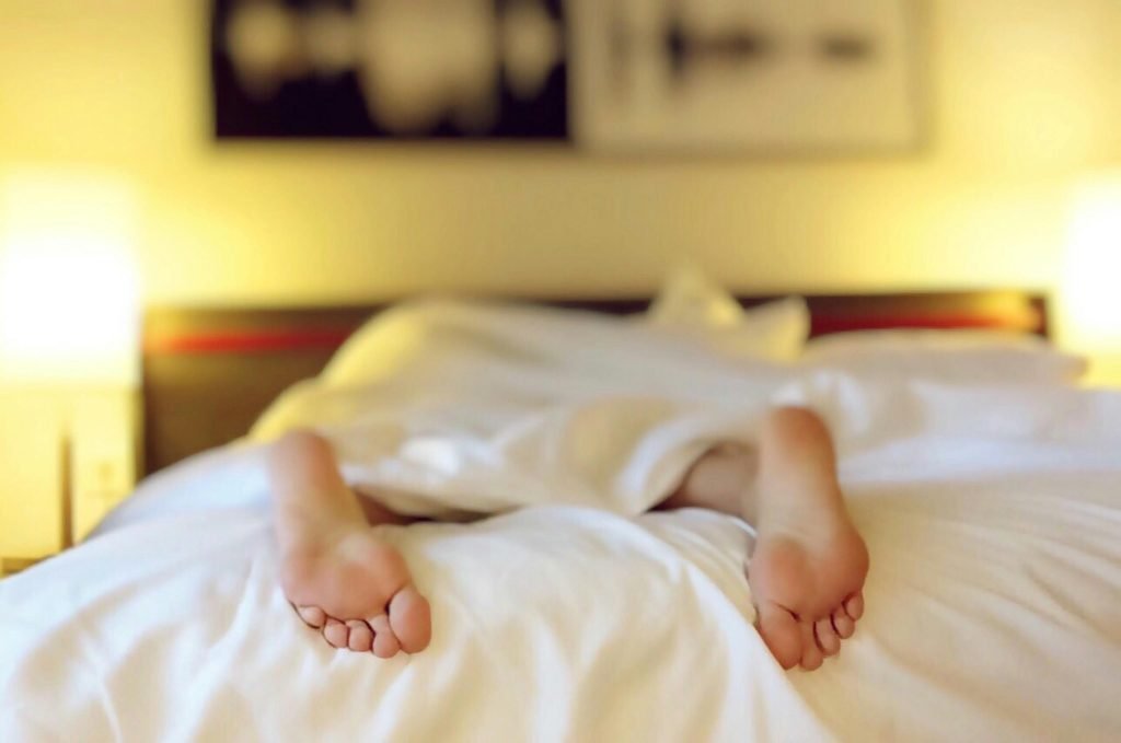 A person relaxing on a bed with feet under white sheets, conveying serenity., hotelería