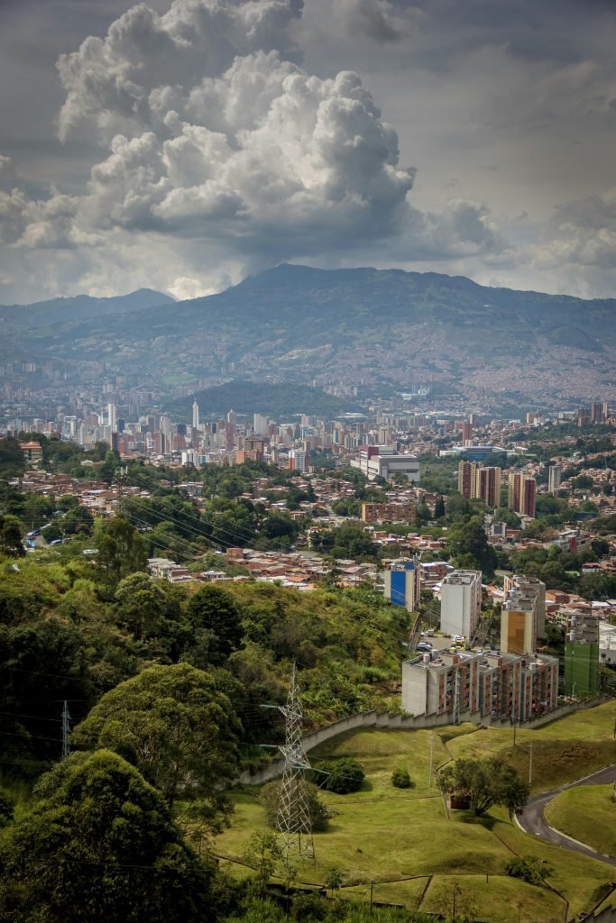 Stunning aerial view of Medellin cityscape under dramatic clouds and lush mountain backdrop., requisitos para viajar a Colombia