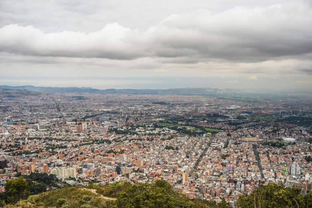 Expansive aerial view of Bogotá, Colombia, showcasing the dense urban cityscape under a cloudy sky., ¿es seguro viajar a Colombia?
