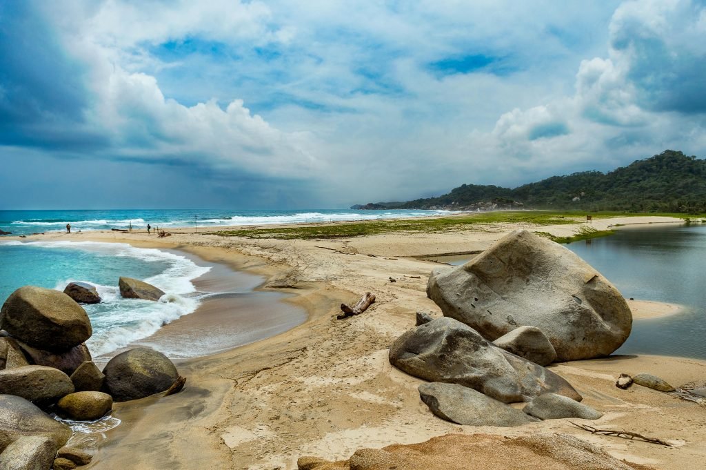 Vibrant beach landscape featuring rocks, waves, and a cloudy sky perfect for travel inspiration., Tayrona