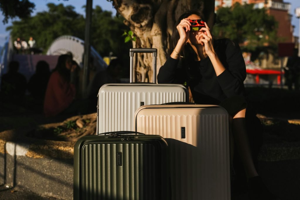 A woman captures moments with a vintage camera beside suitcases outdoors. Perfect for travel themes., equipaje