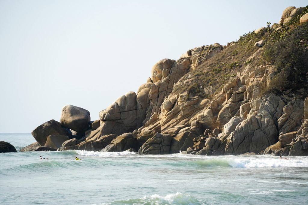 Dramatic ocean waves hit the rocky cliffs of Barra de la Cruz, Oaxaca, under the bright sun., Tayrona
