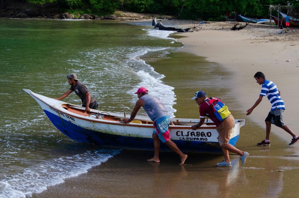 Four men pushing a fishing boat into the sea on a sandy beach in Rio Caribe, Venezuela., capurganá