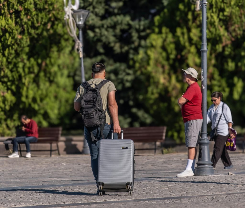 A man with a suitcase and backpack strolling in a sunny park in İzmir, Türkiye., equipaje