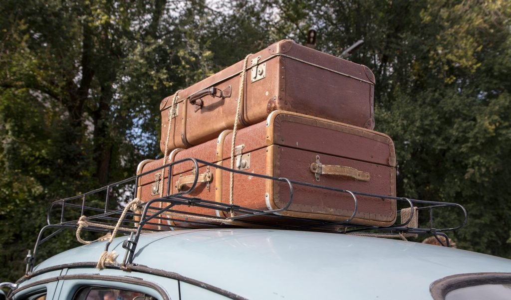 Stack of vintage suitcases secured on a classic car roof rack for an outdoor road trip., equipaje