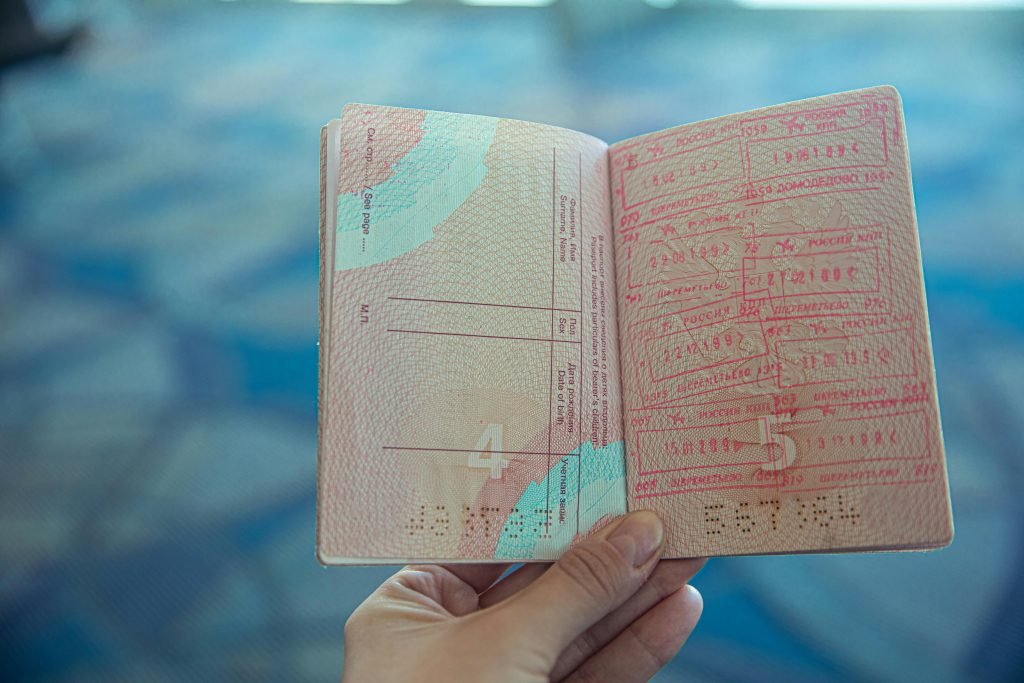 Close-up view of an open passport displaying various travel stamps in an airport setting., visados