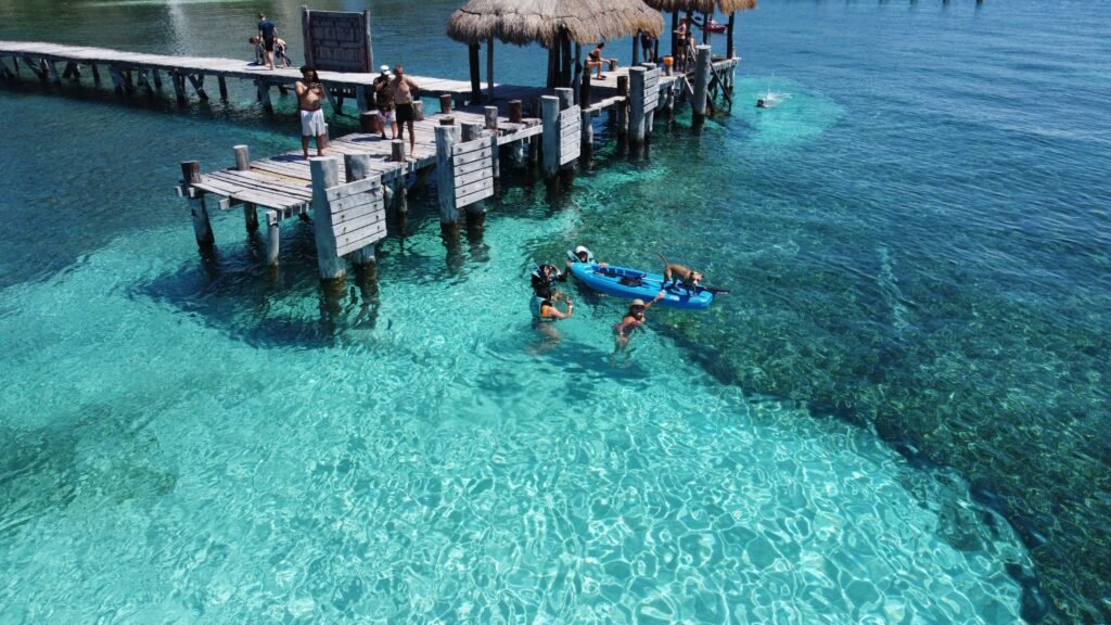 People enjoying a sunny day at Isla Mujeres pier with clear water and vibrant scenery. islas del rosario