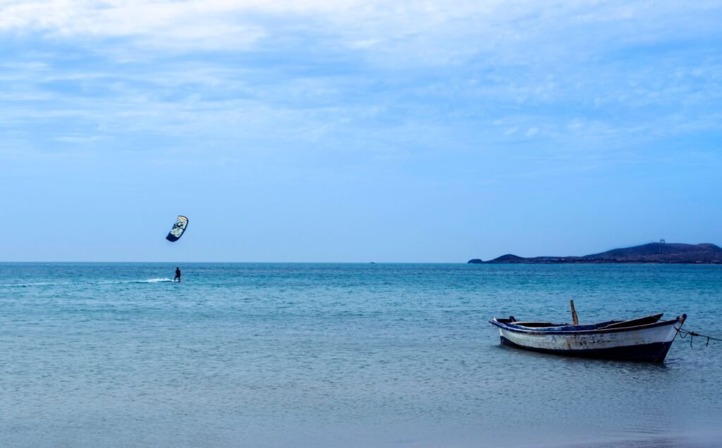 Amazing view of distant kite surfer practicing on blue sea near moored old boat in peaceful resort, Guajira