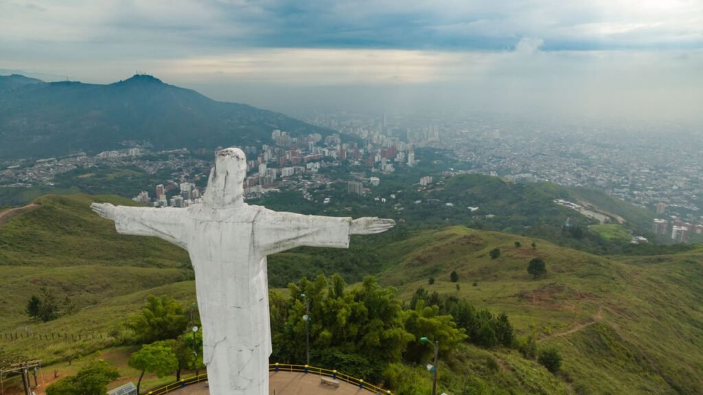 Aerial shot of Christ the Redeemer statue overlooking a cityscape and lush green hills., Cali