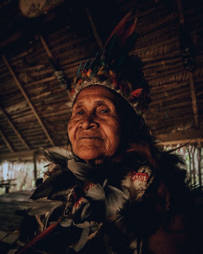 Elderly indigenous woman wearing traditional feather headdress in an Amazonian hut., Leticia