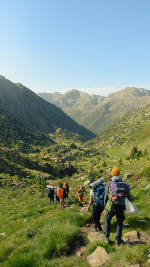 A group of hikers descends a lush mountain trail surrounded by stunning valleys under a clear blue sky., Cali