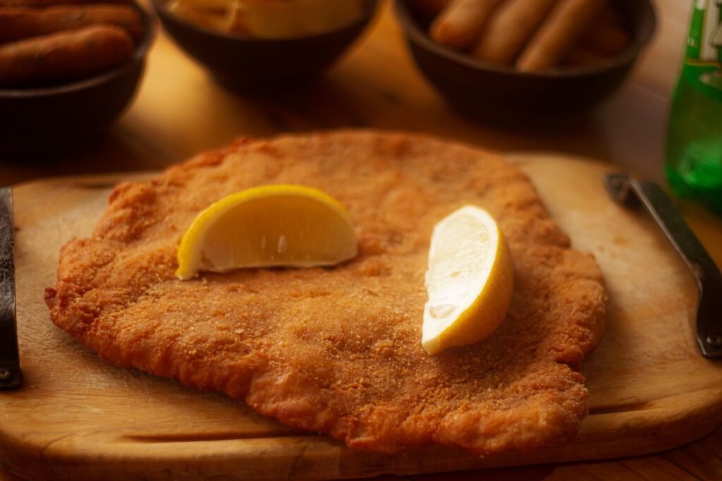 Golden-brown schnitzel topped with lemon wedges on a wooden board, perfect for food photography., Cali