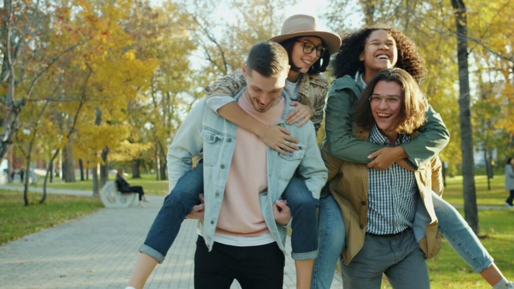 Group of young adults having fun with piggyback rides in a sunny park, highlighting friendship., Colombia todo incluido