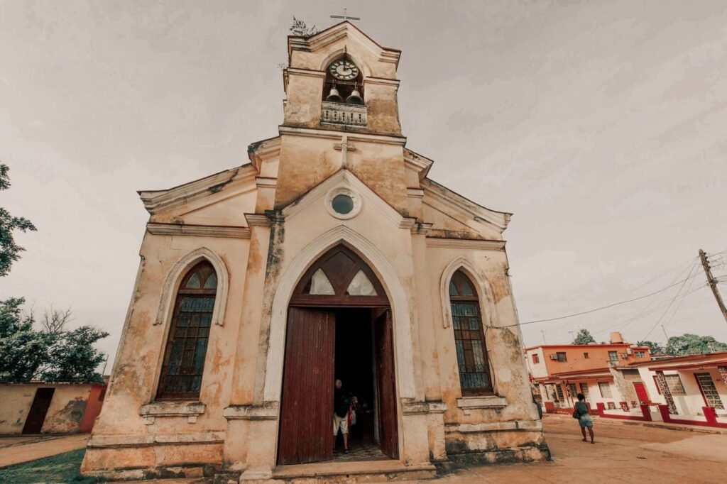 A historic, weathered church with a clock tower stands against a cloudy sky, reflecting vintage architecture., Guaviare