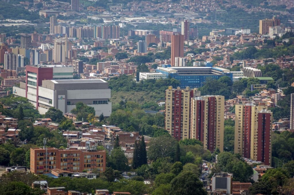 Aerial view of a bustling urban cityscape with tall buildings surrounded by greenery. cuanto cuesta un viaje a colombia