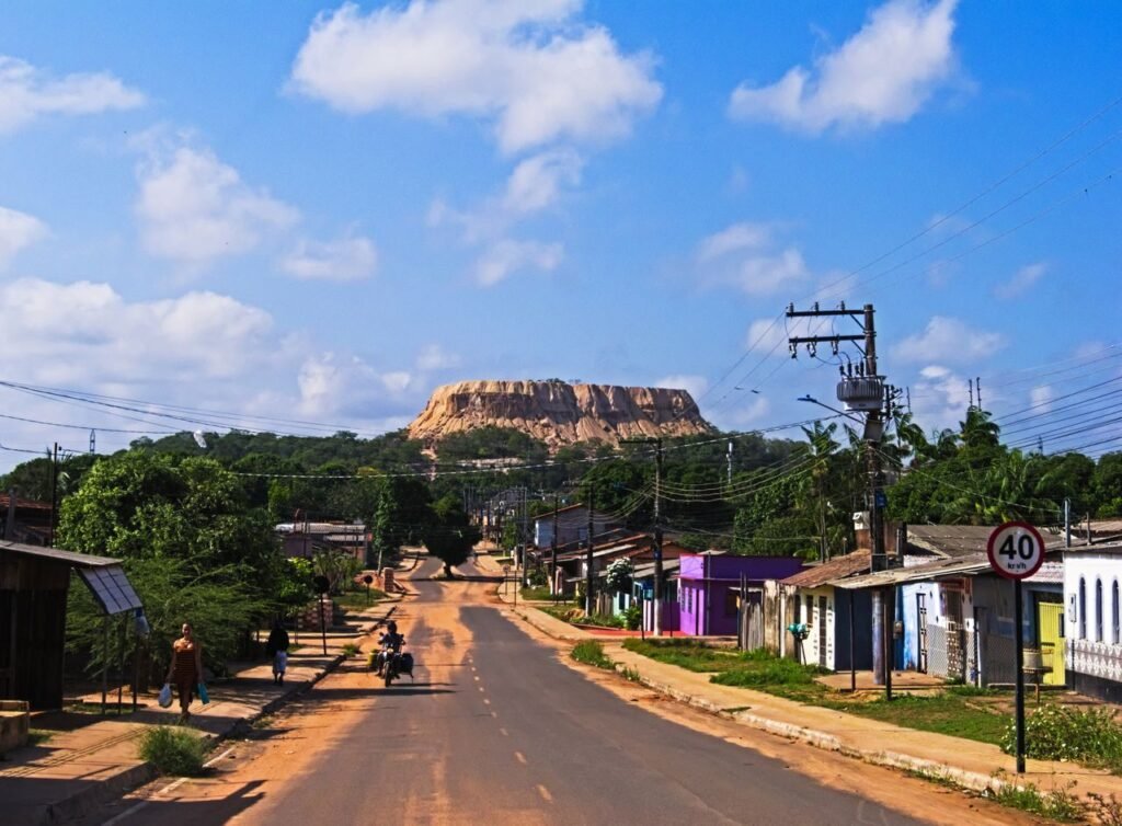 A vibrant town road with power lines leads to a majestic mountain under a blue sky., Guaviare
